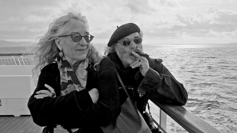 Pino Bertelli e Paola Grillo abbracciati sulla nave per l’Isola d’Elba, con il mare alle spalle, durante le riprese del documentario diretto da Antonio Manco